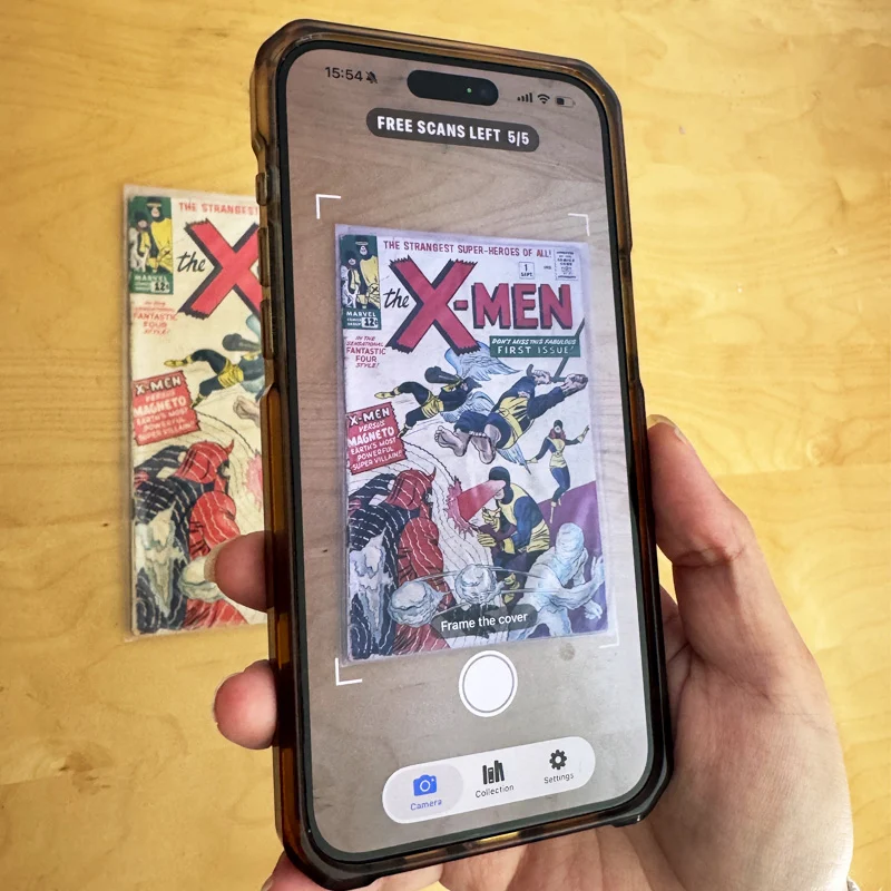A hand holding an iPhone running Comic Scry, framing an X-Men #1 cover lying on a wood table. The on-screen reticle reads "Frame the cover" and a banner shows five free scans left.